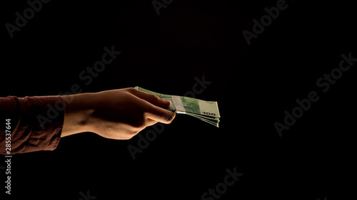 Man hand giving euro banknotes, black background, financial fraud, corruption