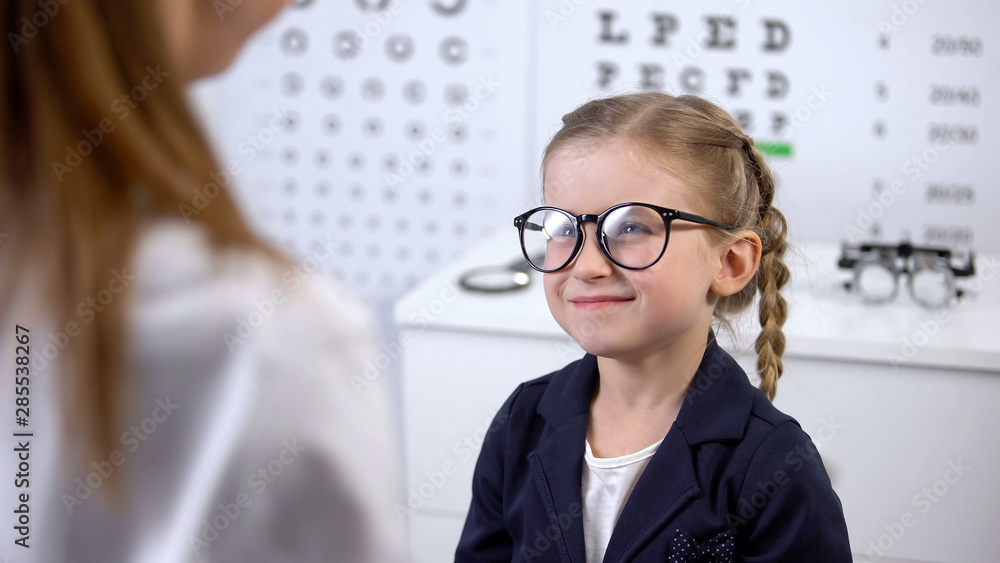 Female optician putting glasses on schoolgirl, little client happy with eyewear Female optician putting glasses on schoolgirl, little client happy with eyewear