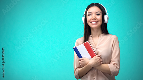Girl listening French audio lessons in headset, book in hands, translations
