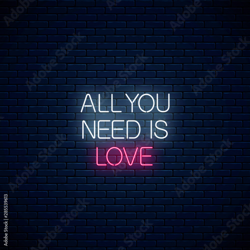 All you need is love - glowing neon inscription phrase on dark brick wall background. Motivation quote in neon style