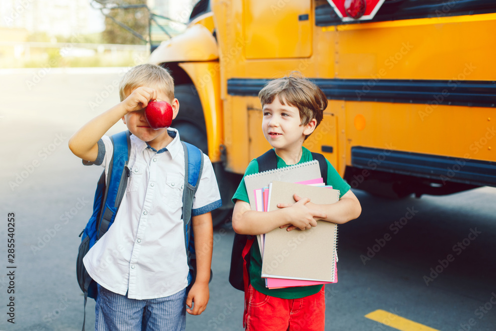 Φωτογραφία Two funny happy Caucasian boys students kids with apples standing near yellow bus on 1 September day