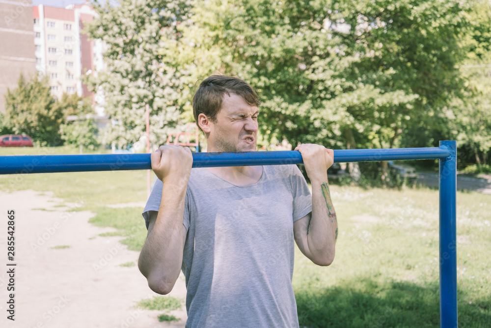 A young handsome man in casual clothes is doing pull up exercise on horizontal bar. fitness, sport, exercising, training and lifestyle concept - young man doing pull ups on horizontal bar outdoors A young handsome man in casual clothes is doing pull up exercise on horizontal bar. fitness, sport, exercising, training and lifestyle concept - young man doing pull ups on horizontal bar outdoors