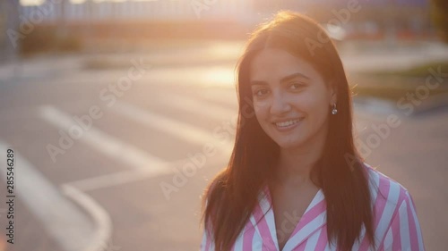 Beautiful young cheerful wooman smiling and playing with hair on the streer at sunset. Closeup portrait of positive girl outdoors in Slow motion photo