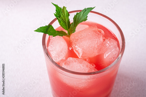 Fresh cold watermelon juice with ice cubes and green mint leaf in glass drink on white background, macro, selective focus