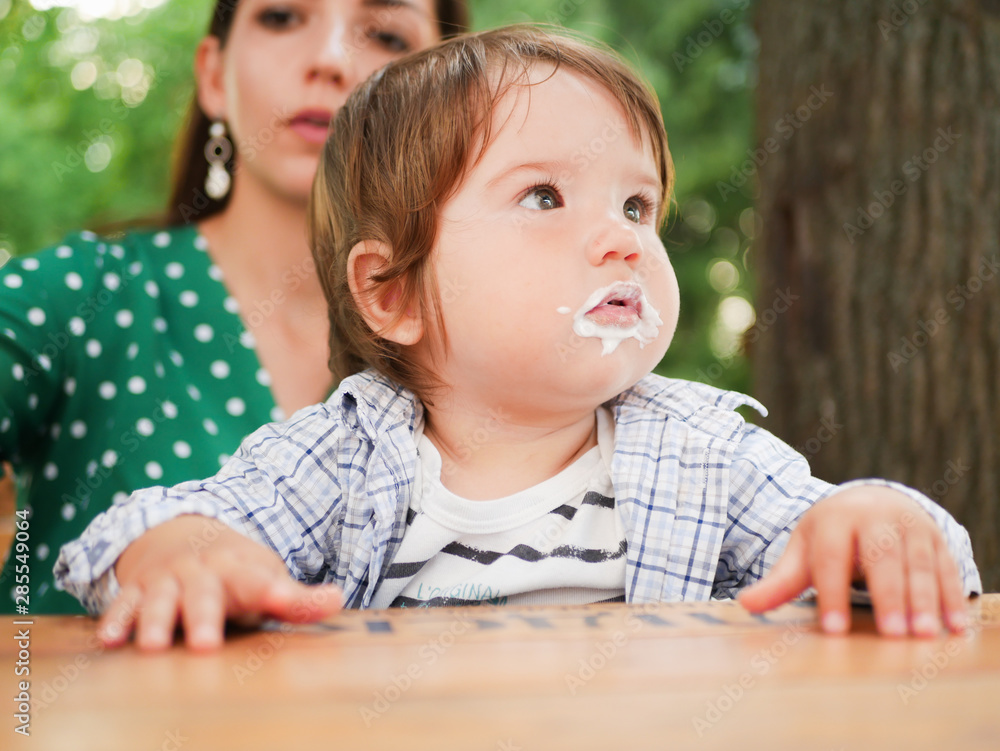 mom feeds her baby on the street. A mother feeds her little baby with a spoon on the street. mouth in food. healthy cottage cheese and yogurd mom feeds her baby on the street. A mother feeds her little baby with a spoon on the street. mouth in food. healthy cottage cheese and yogurd