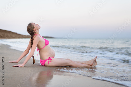 Young pregnant woman is relaxing on the seashore. Breathing sea. Deserted beach, pre sunset time