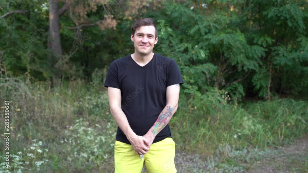A young handsome man in casual clothes is smiling and looking at camera in the forest. A young handsome man in casual clothes is smiling and looking at camera in the forest.