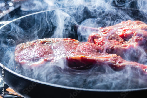 Smoke and steam rise from a beaf steak on grill pan. photo