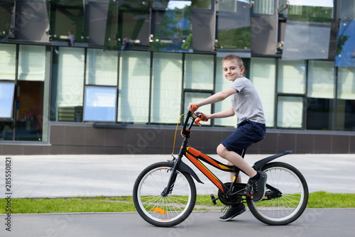 Schoolboy rides a bicycle. Summer holidays. Urban background