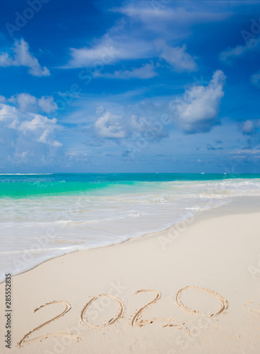 New Year 2020 handwritten on the sandy beach with ocean wave