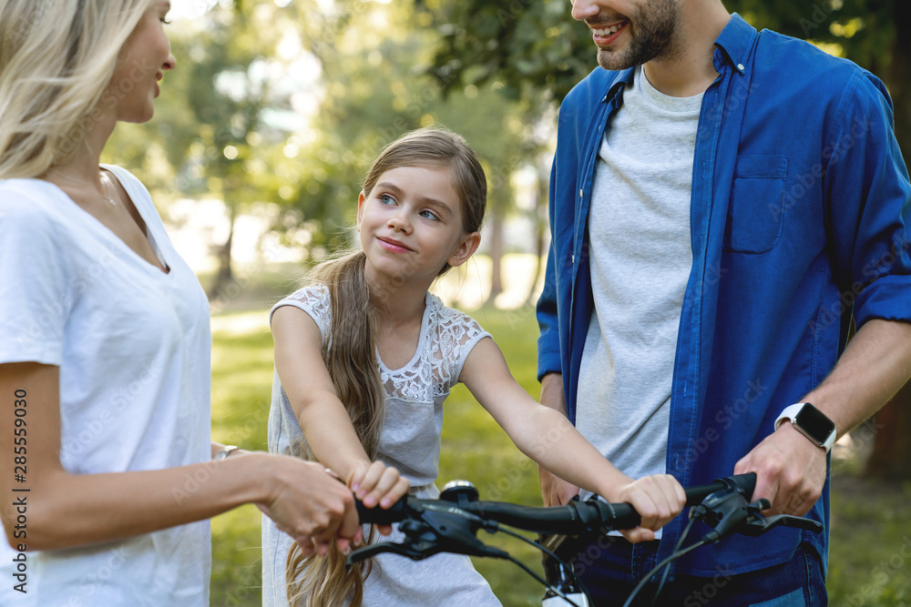 Close up shot of parents learning their little cute daughter how to ride a bike Close up shot of parents learning their little cute daughter how to ride a bike