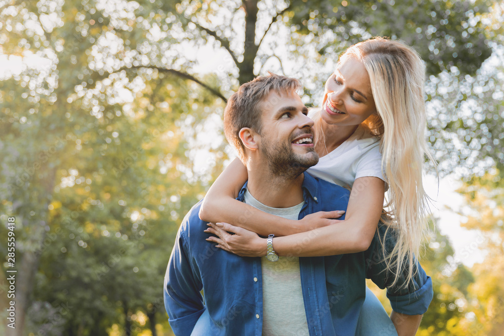 Low angle view of young beautiful couple piggybacking and having fun outdoors Low angle view of young beautiful couple piggybacking and having fun outdoors