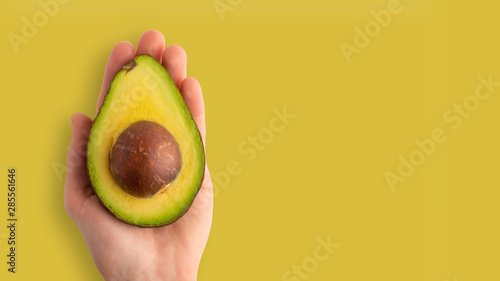 Avocado in a female hand is isolated on a yellow background, for design, horizontal photo, banner