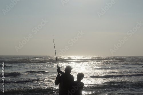 father and son, in front of the sea fishing while is the sunset