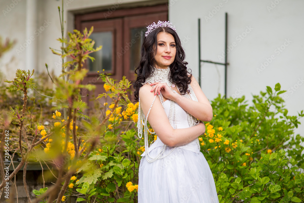 Sensual and Sexy Caucasian Bride With Diadem Posing In Flowers Garden Outdoors. Wearing Beads Necklace.