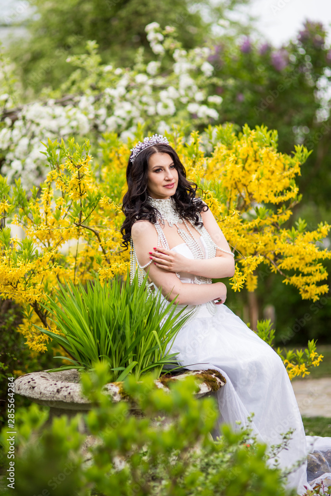 Caucasian Brunette in Flowers Garden Outdoors.Wearing Diadem and Necklace Caucasian Brunette in Flowers Garden Outdoors.Wearing Diadem and Necklace
