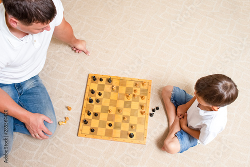 Closeup of Little Boy Playing Chess with his Father Together. Sitting Closely on Floor and Thinking.