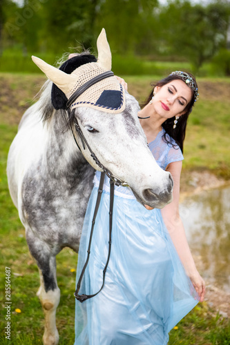 Caucasian Brunette With Tiara Walking with Horse Outdoors. Against Nature Background. © danmorgan12