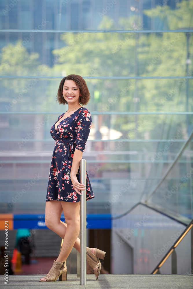 Beautiful biracial woman in floral print dress poses at top of mass transit entrance Beautiful biracial woman in floral print dress poses at top of mass transit entrance