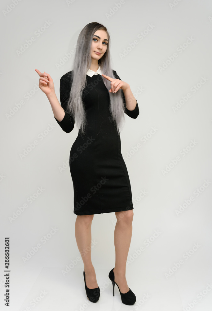 Full length studio portrait of a pretty manager girl with long beautiful hair in a black dress on a white background. He stands in front of the camera, smiles, shows his hands. Full length studio portrait of a pretty manager girl with long beautiful hair in a black dress on a white background. He stands in front of the camera, smiles, shows his hands.