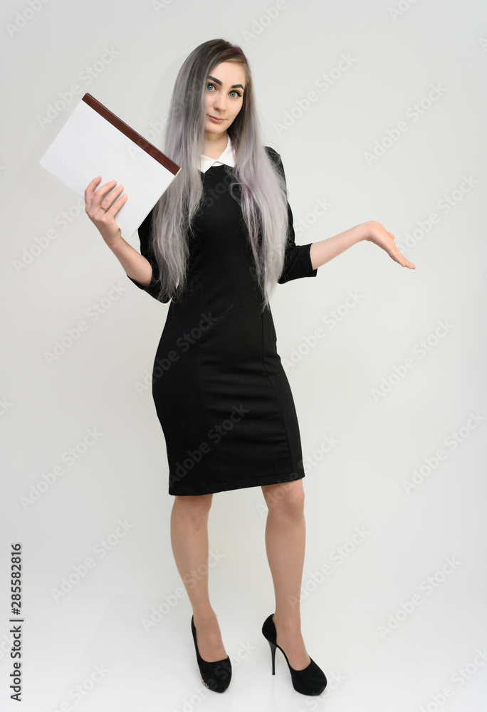 Full length studio portrait of a pretty manager girl with long beautiful hair in a black dress with a folder in her hands on a white background. He stands in front of the camera, smiles, shows hands. Full length studio portrait of a pretty manager girl with long beautiful hair in a black dress with a folder in her hands on a white background. He stands in front of the camera, smiles, shows hands.