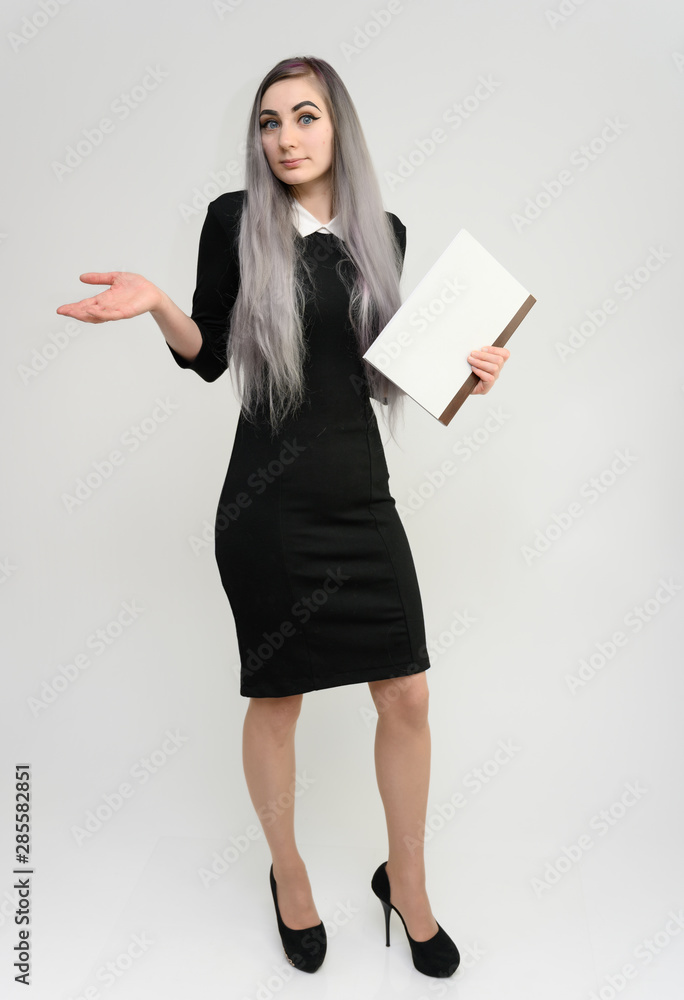 Full length studio portrait of a pretty manager girl with long beautiful hair in a black dress with a folder in her hands on a white background. He stands in front of the camera, smiles, shows hands. Full length studio portrait of a pretty manager girl with long beautiful hair in a black dress with a folder in her hands on a white background. He stands in front of the camera, smiles, shows hands.