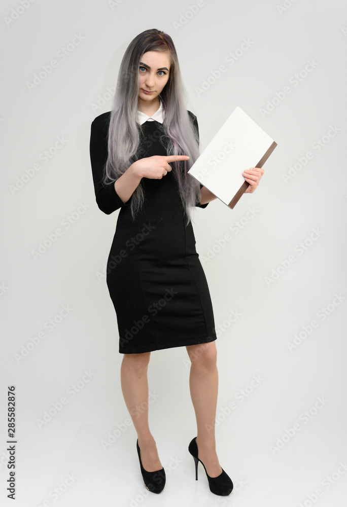 Full length studio portrait of a pretty manager girl with long beautiful hair in a black dress with a folder in her hands on a white background. He stands in front of the camera, smiles, shows hands. Full length studio portrait of a pretty manager girl with long beautiful hair in a black dress with a folder in her hands on a white background. He stands in front of the camera, smiles, shows hands.