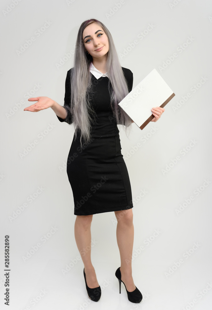 Full length studio portrait of a pretty manager girl with long beautiful hair in a black dress with a folder in her hands on a white background. He stands in front of the camera, smiles, shows hands. Full length studio portrait of a pretty manager girl with long beautiful hair in a black dress with a folder in her hands on a white background. He stands in front of the camera, smiles, shows hands.