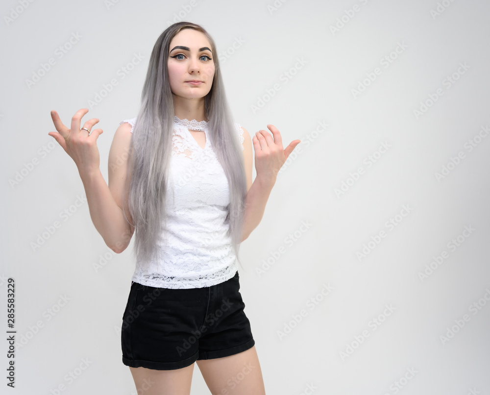 Studio portrait on the waist of a pretty manager girl with long beautiful hair in a white T-shirt and black shorts on a white background. He stands straight, smiles, shows with his hands. Studio portrait on the waist of a pretty manager girl with long beautiful hair in a white T-shirt and black shorts on a white background. He stands straight, smiles, shows with his hands.
