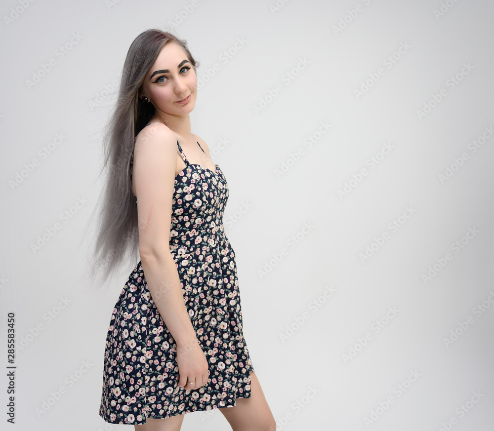 Studio portrait of a knee-length of a pretty student girl with long beautiful hair in a beautiful color dress on a white background. He stands straight, smiles, shows with his hands. Studio portrait of a knee-length of a pretty student girl with long beautiful hair in a beautiful color dress on a white background. He stands straight, smiles, shows with his hands.