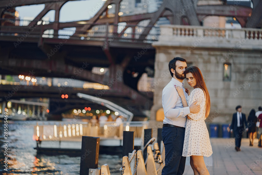 beautiful long-haired girl in summer dress with her handsome husband in white shirt and pants walking in a evening Chicago