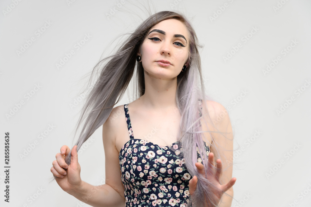 Studio portrait of a pretty student girl with long beautiful hair in a beautiful color dress on a white background. He stands straight, smiles, shows with his hands.