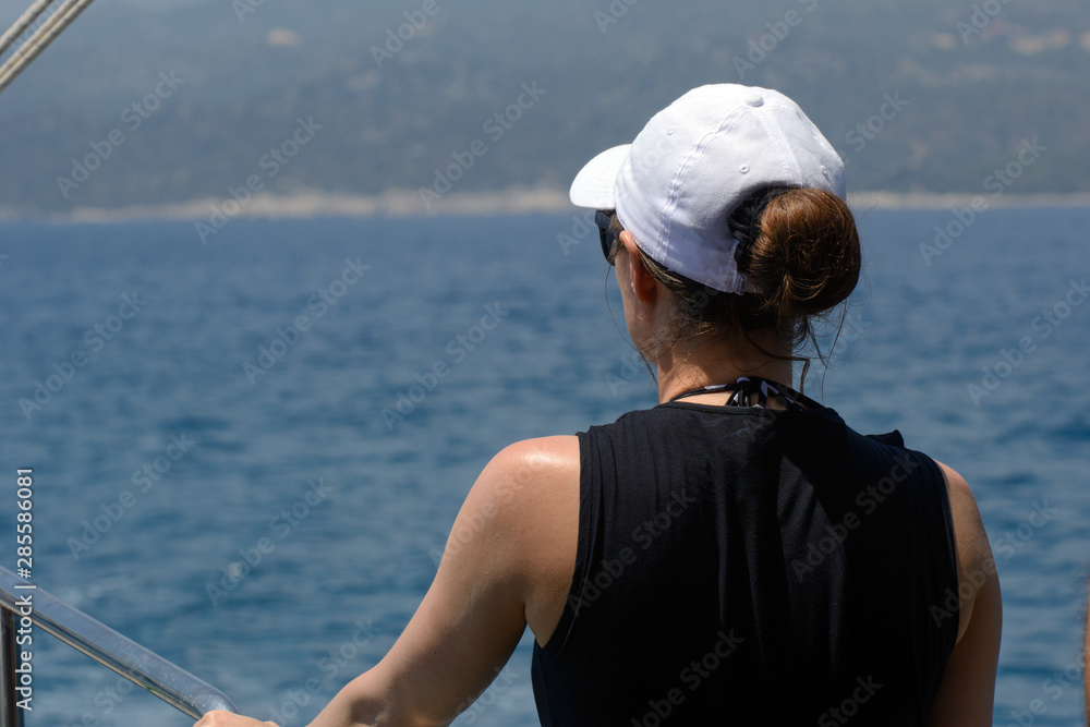 woman in a black t-shirt and white cap is yoing aboard a yacht. woman looks at the mediterranean sea. Concept - travel, make plans woman in a black t-shirt and white cap is yoing aboard a yacht. woman looks at the mediterranean sea. Concept - travel, make plans