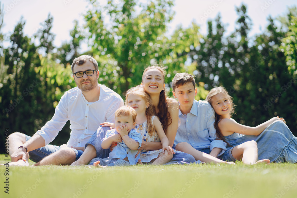 beautiful long-haired mother in a long blue dress in sunny summer forest walks with his beautiful children and handsome man