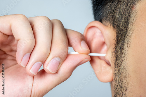 A young man asia using a stick of cotton swab for ears cleaning. Daily hygiene. Light gray background. Close up.