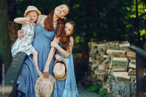 beautiful long-haired mother in a long blue dress in sunny summer forest walks with his beautiful daughters