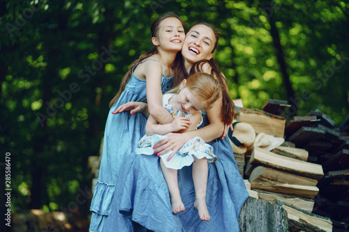 beautiful long-haired mother in a long blue dress in sunny summer forest walks with his beautiful daughters