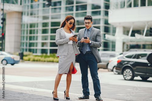 Handsome businessman in a city. Businessman in a glasses. Business couple in a summer city. Man and woman standing with phone. Pretty girl in a dress with her parther.