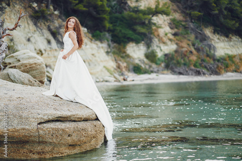 Beautiful long-haired bride in a magnificent white dress walking near water