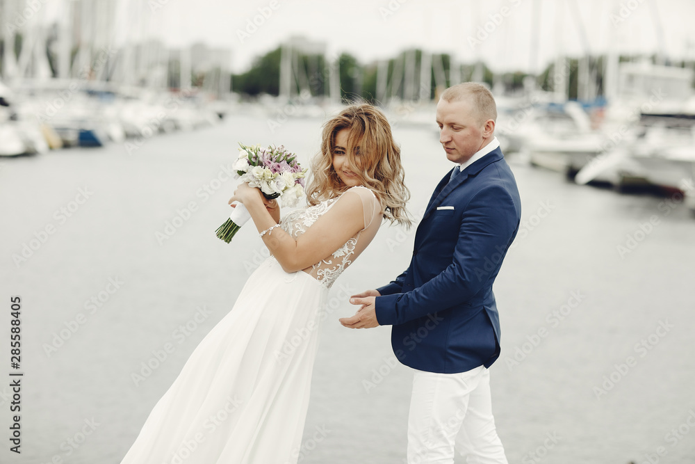 Naklejka premium Beautiful bride in a long white dress. Handsome fiance in a blue suit. Couple near ocean