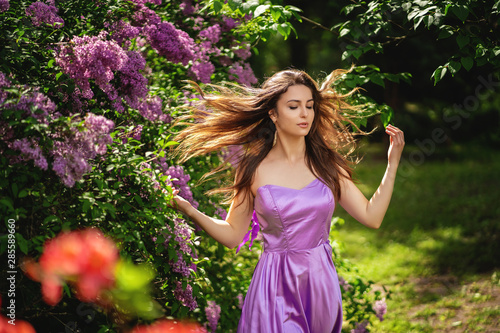 Authentic woman near a blossoming lilac tree. Her hair flutters in the wind