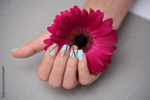Woman hand with trendy nail art manicure holding gerberas flower on grey background