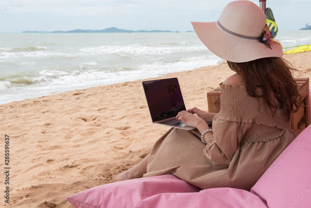 Traveller woman sitting on beach couch using Laptop computer searching information, summer beach holiday vacation concept. 