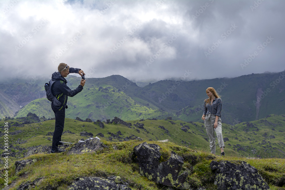 Green alpine meadow on the slopes and mountains in the fog. Cloudy day in the mountains. A man photographs a girl on a beautiful background.