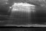 Sunrays with dark clouds in the background and Trasimeno lake (Umbria, Italy) below