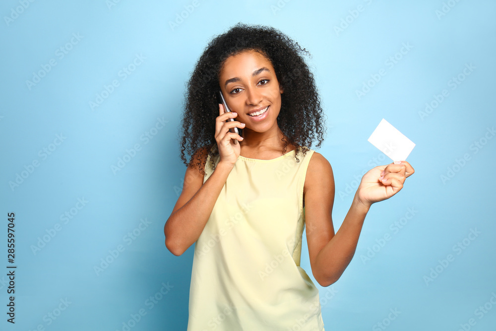Portrait of beautiful African-American woman with business card talking by mobile phone on color background Portrait of beautiful African-American woman with business card talking by mobile phone on color background