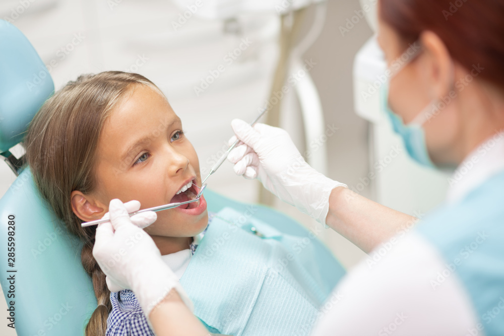 Experienced child dentist examining cute blonde schoolgirl