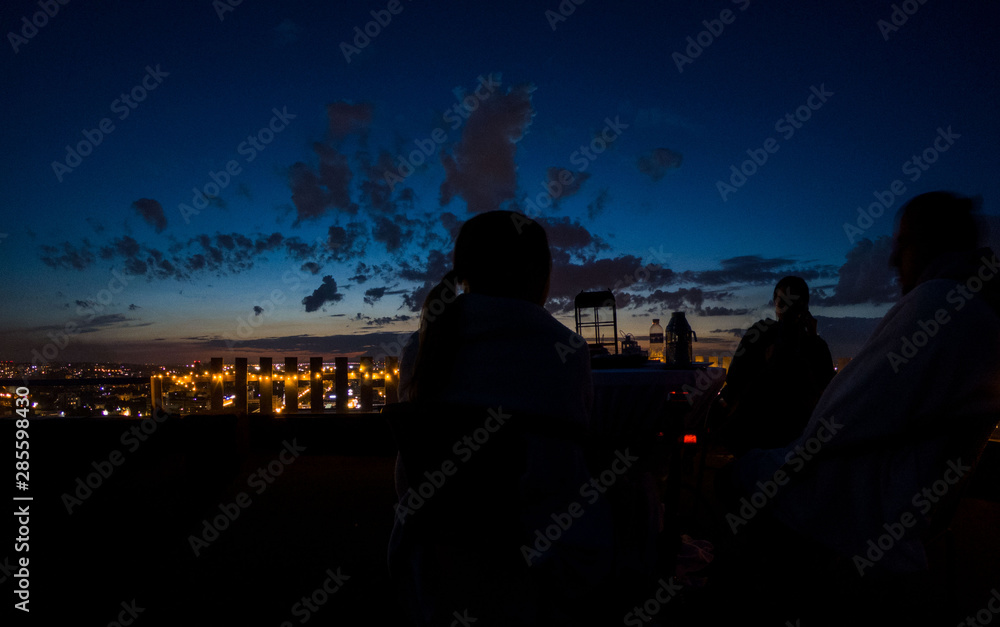 Silhouettes of people sitting on the roof and looking at the city and the sky