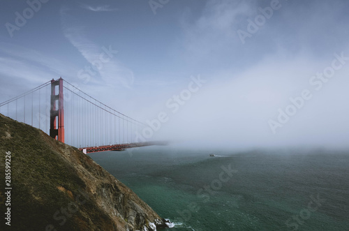 Golden Gate Bridge is shown in a fog with a boat crossing the bay