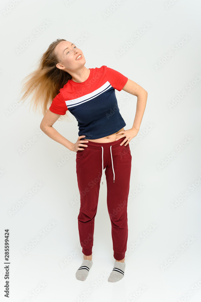 Full length studio portrait of a pretty young happy blonde woman in a tracksuit on a white background. He smiles, talks, shows with his hands, moves, shows emotions.
